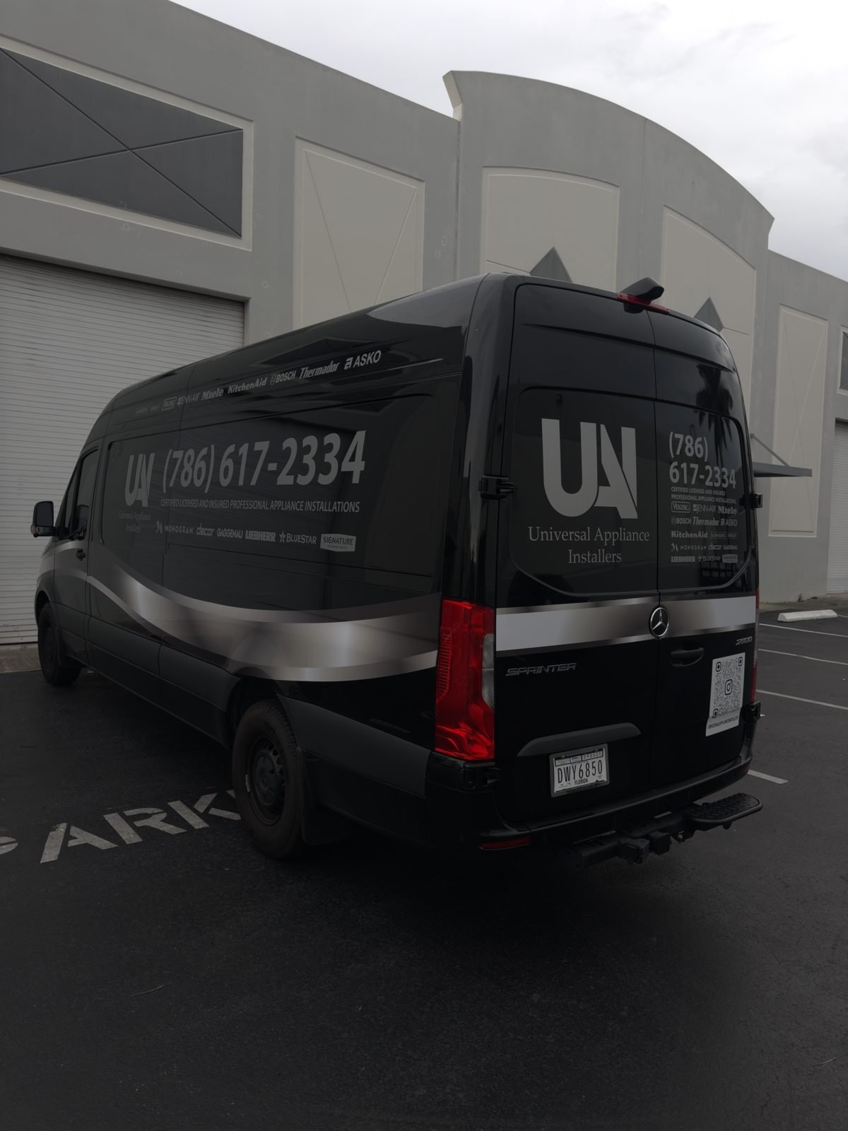 Rear doors of a black Sprinter van with logo and phone number